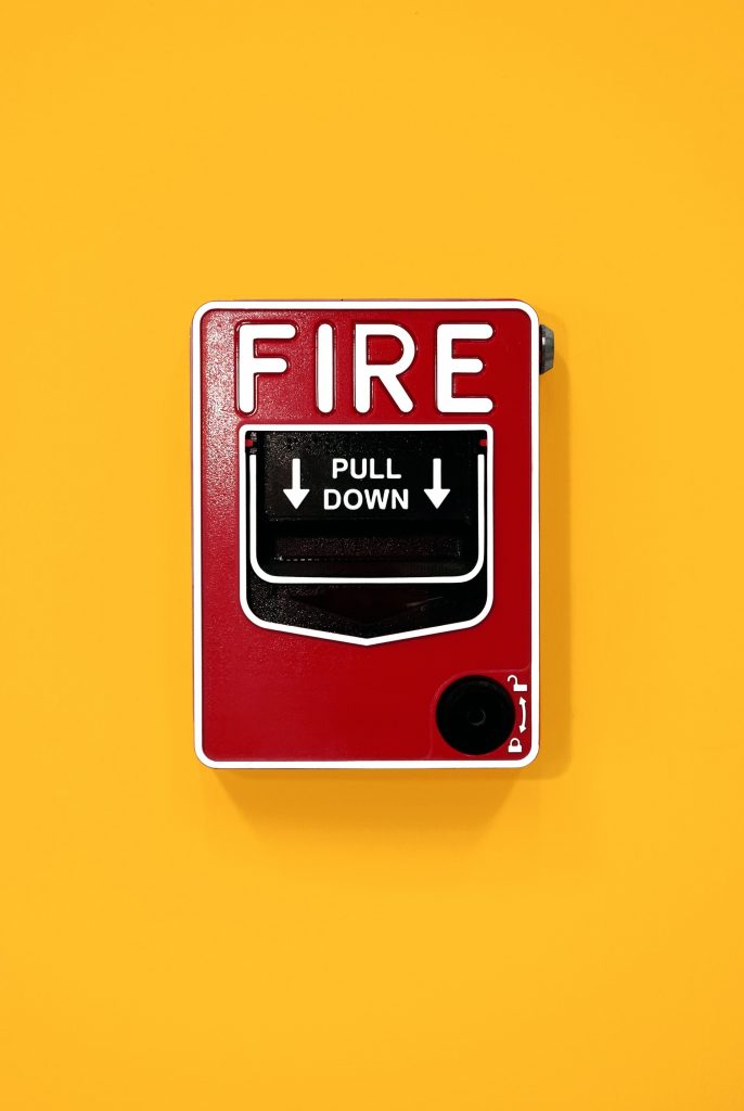 Red fire alarm pull station on yellow background